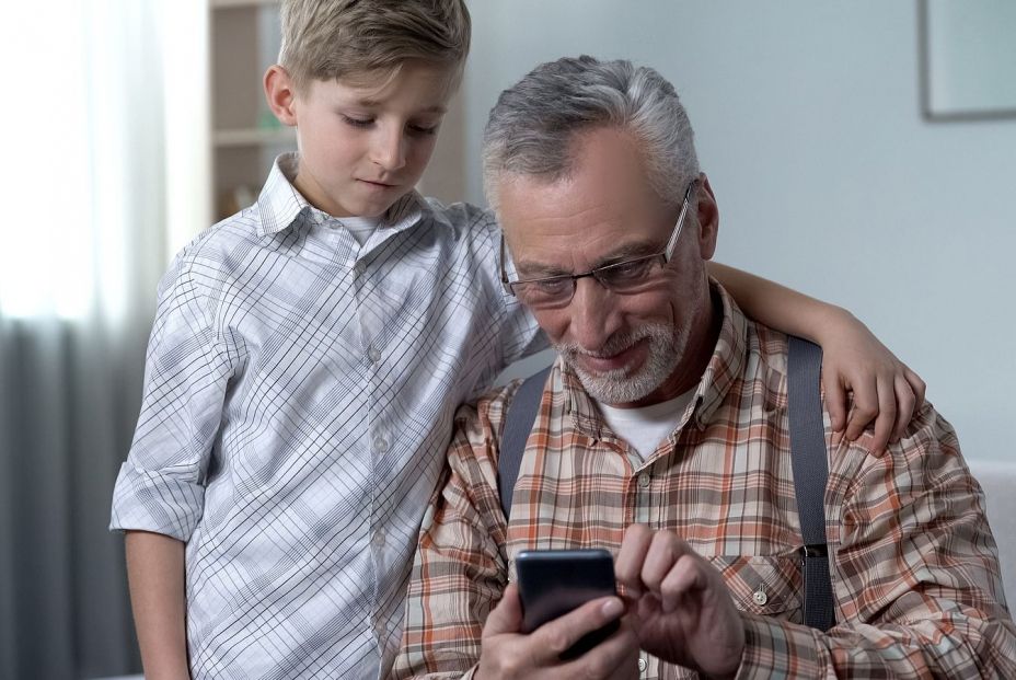 Un adulto mayor con su nieto usando el móvil Bigstock.