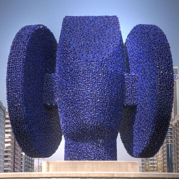 Torre Miramar Esta peculiar lista comienza con un mirador que se alza majestuoso sobre el túnel de la avenida Cataluña, pero desde el que curiosamente apenas se alcanza para ver el mar que era la idea con la que fue construido. Se trata de la Torre Miramar. Versatilidad aparte, este es uno de los monumentos o edificios que cada año aparece en las listas de los más feos no solo de Valencia, sino también de España. En total 45 metros de altura en forma de una torre de hormigón coronada por una caja de vidrio de color oscuro. A pocos minutos de la anterior se encuentra una curiosa escultura que también forma parte de los rankings de dudoso gusto estético. Tanto es así que incluso en los primeros días tras su instalación no fueron pocos los vecinos que no veían el sentido de esta instalación ya que consideraban que eran los restos sin recoger de las obras de remodelación vial de la zona. Un amasijo de hierro que en realidad es una escultura de arte contemporáneo y que se alza sobre una rotonda. 